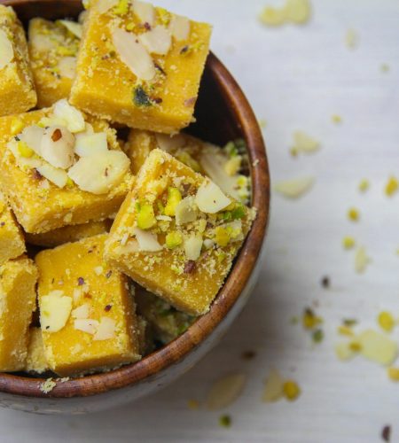 Top view of delicious Indian besan barfi garnished with almonds and pistachios, served in a wooden bowl.